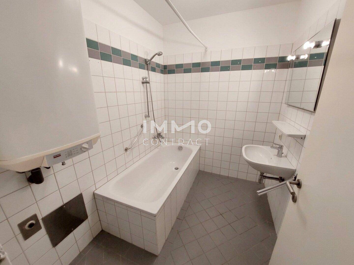Badezimmer mit Badewanne, Dusche, Waschbecken und weißen Fliesen mit farbigem Akzentstreifen.