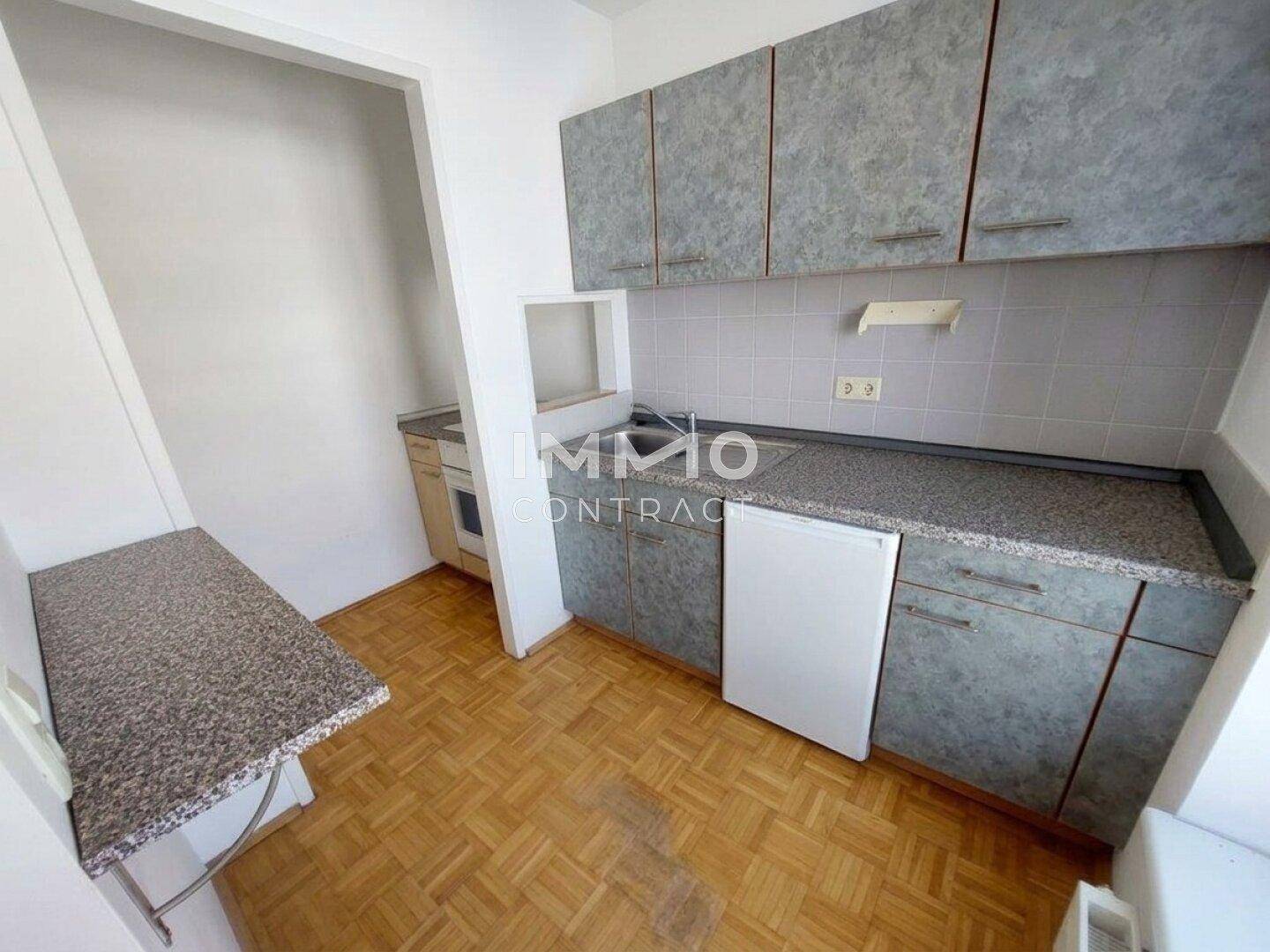 Funktionale Küchenzeile mit grauen Schränken, Granit-Arbeitsplatte und integriertem Kühlschrank.