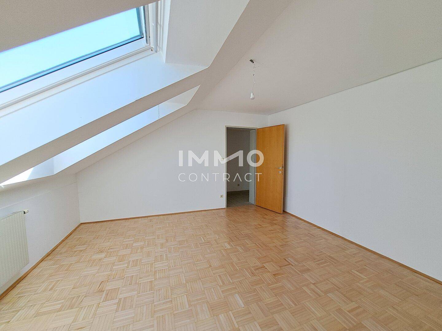 Dachgeschosszimmer mit Parkettboden, schrägen Wänden und einem großen Dachfenster für viel Licht.