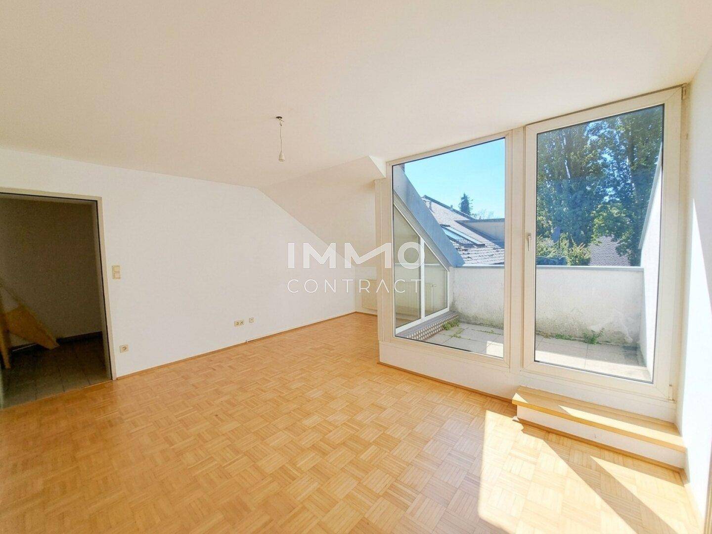 Geräumiges Wohnzimmer mit Parkettboden, viel Tageslicht und Zugang zu einem kleinen Außenbereich.