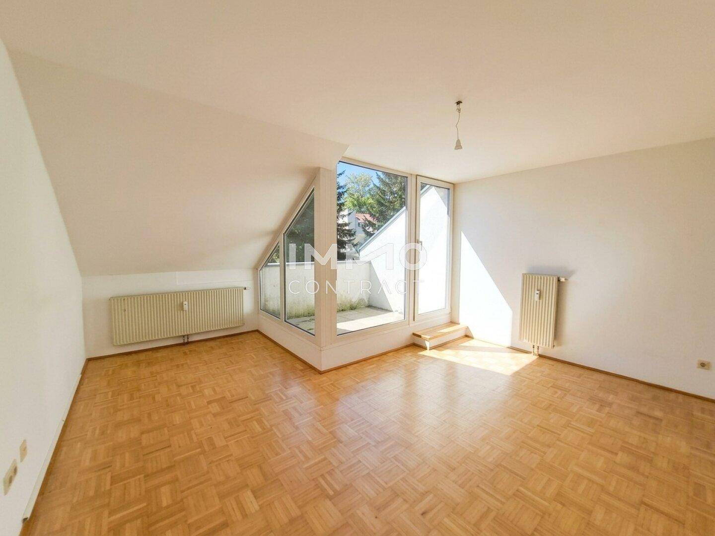 Helles Zimmer im Dachgeschoss mit Parkettboden, schrägen Wänden und großem Fenster.