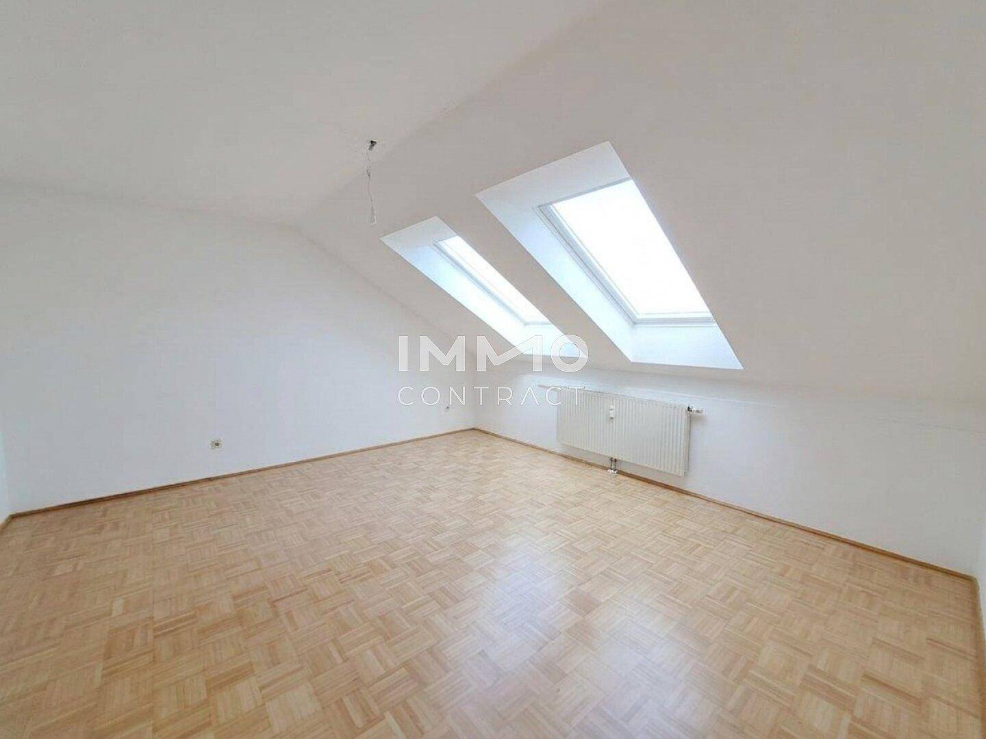 Helles Dachgeschosszimmer mit Parkettboden, schrägen Wänden und zwei Dachfenstern.