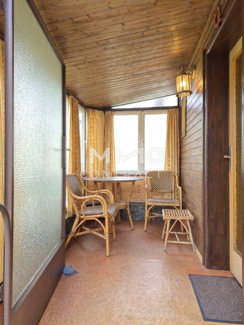 Gemütlicher Wintergarten mit Rattanmöbeln, Holzverkleidung und Blick nach draußen.