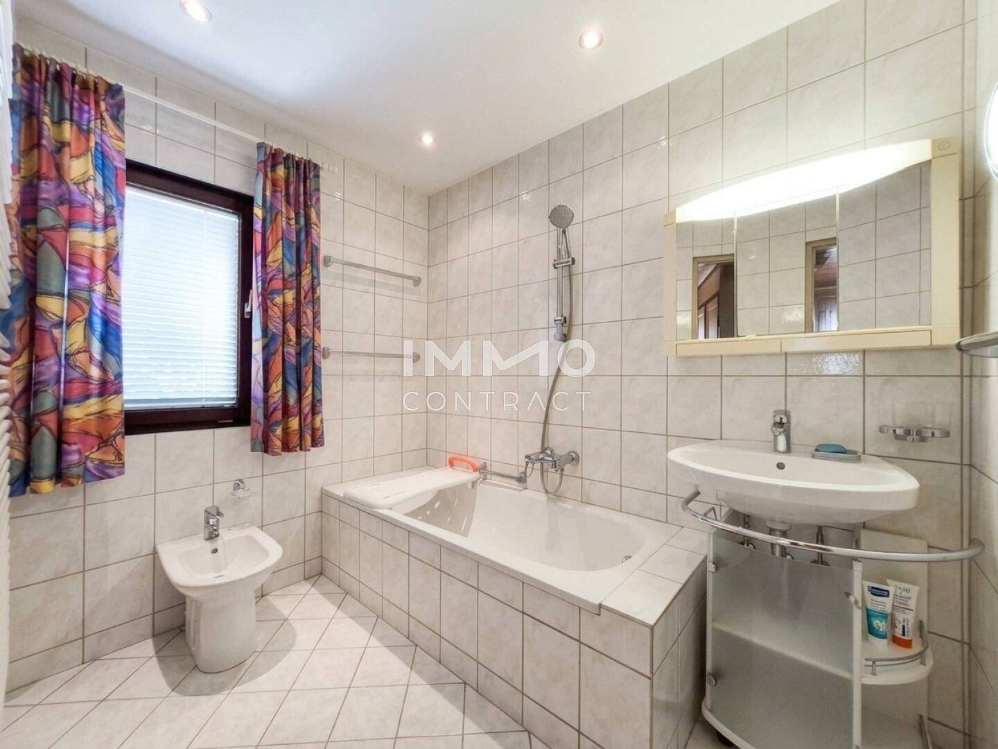 Gefliestes Badezimmer mit Badewanne, Bidet, Waschbecken und Fenster.