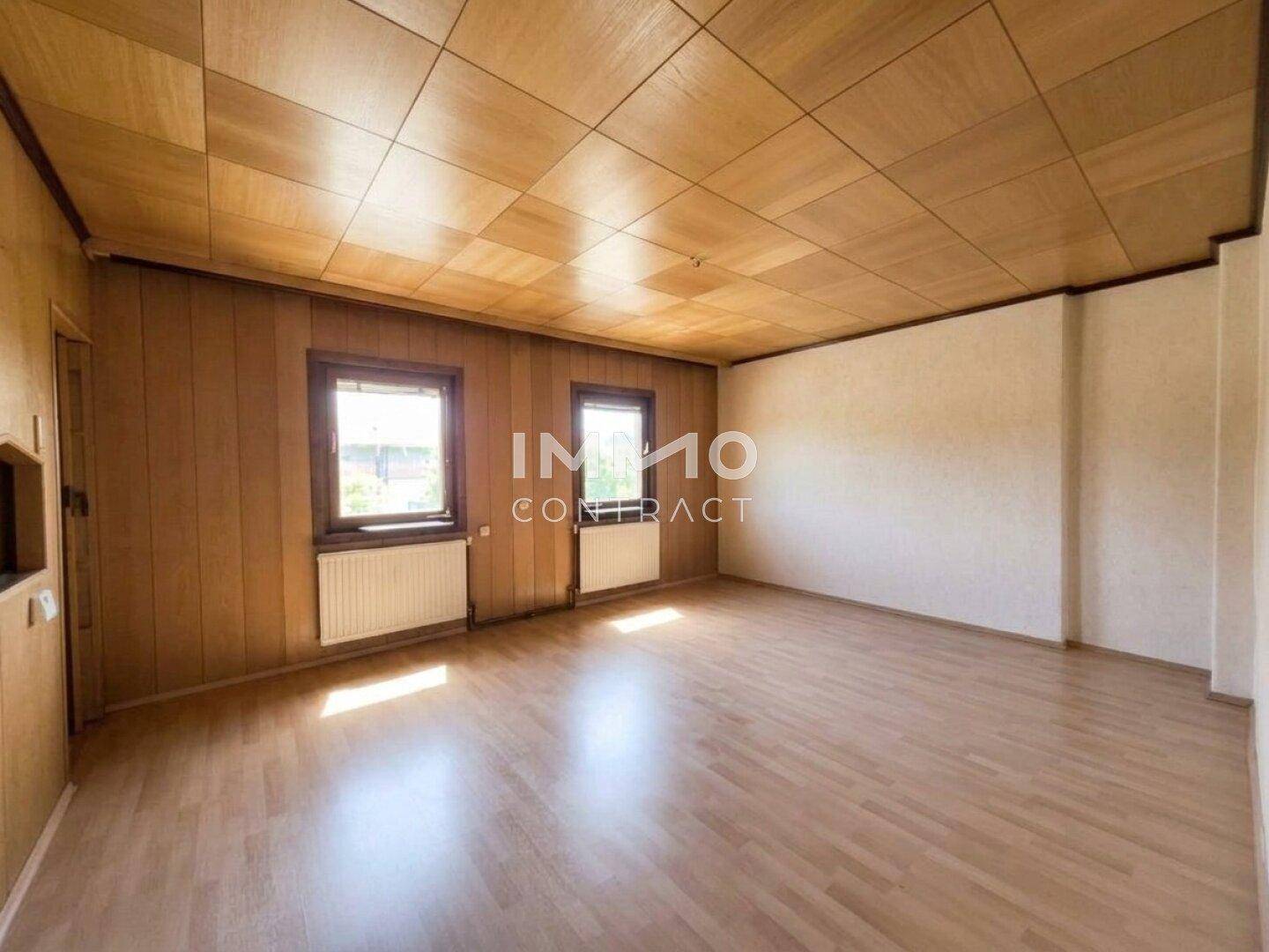 Geräumiger, leerer Raum mit Holzvertäfelung, Laminatboden und zwei Fenstern.