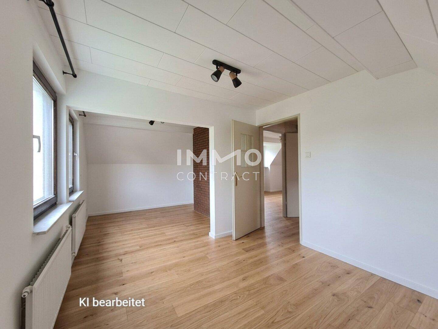 Heller, leerer Raum mit Holzboden, weißen Wänden und sichtbaren Heizkörpern.
