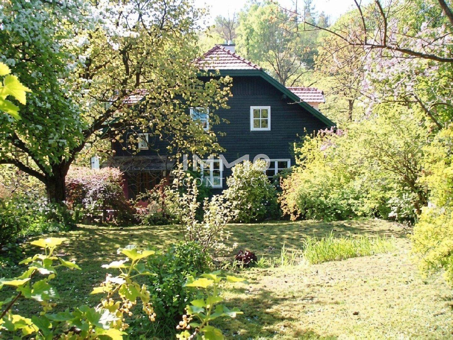 Idyllisches Holzhaus eingebettet in einen weitläufigen, grünen Garten mit blühenden Bäumen.