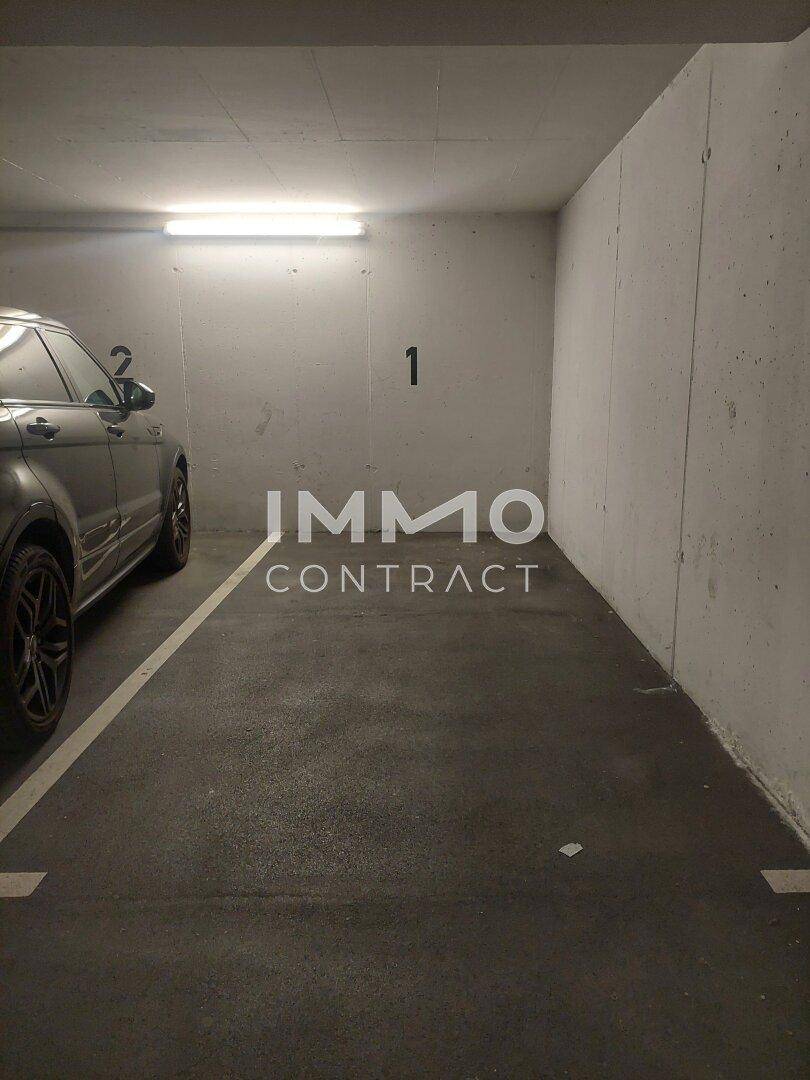 Einzelner Parkplatz in einer Tiefgarage mit Betonwänden und Deckenbeleuchtung.
