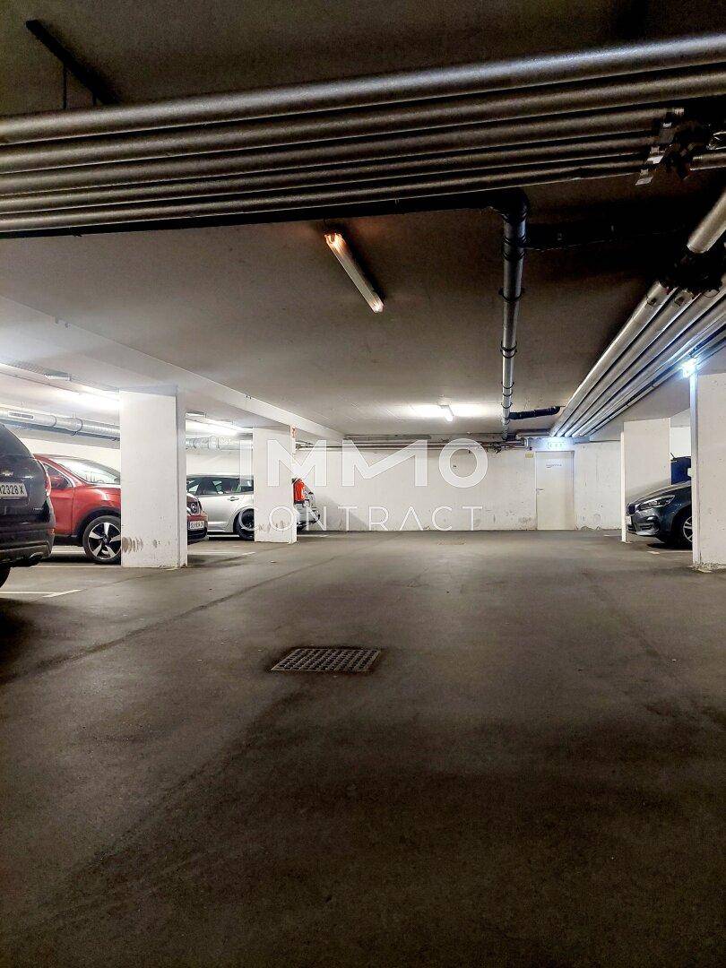 Geräumige Tiefgarage mit mehreren Parkplätzen und sichtbaren Versorgungsleitungen an der Decke.