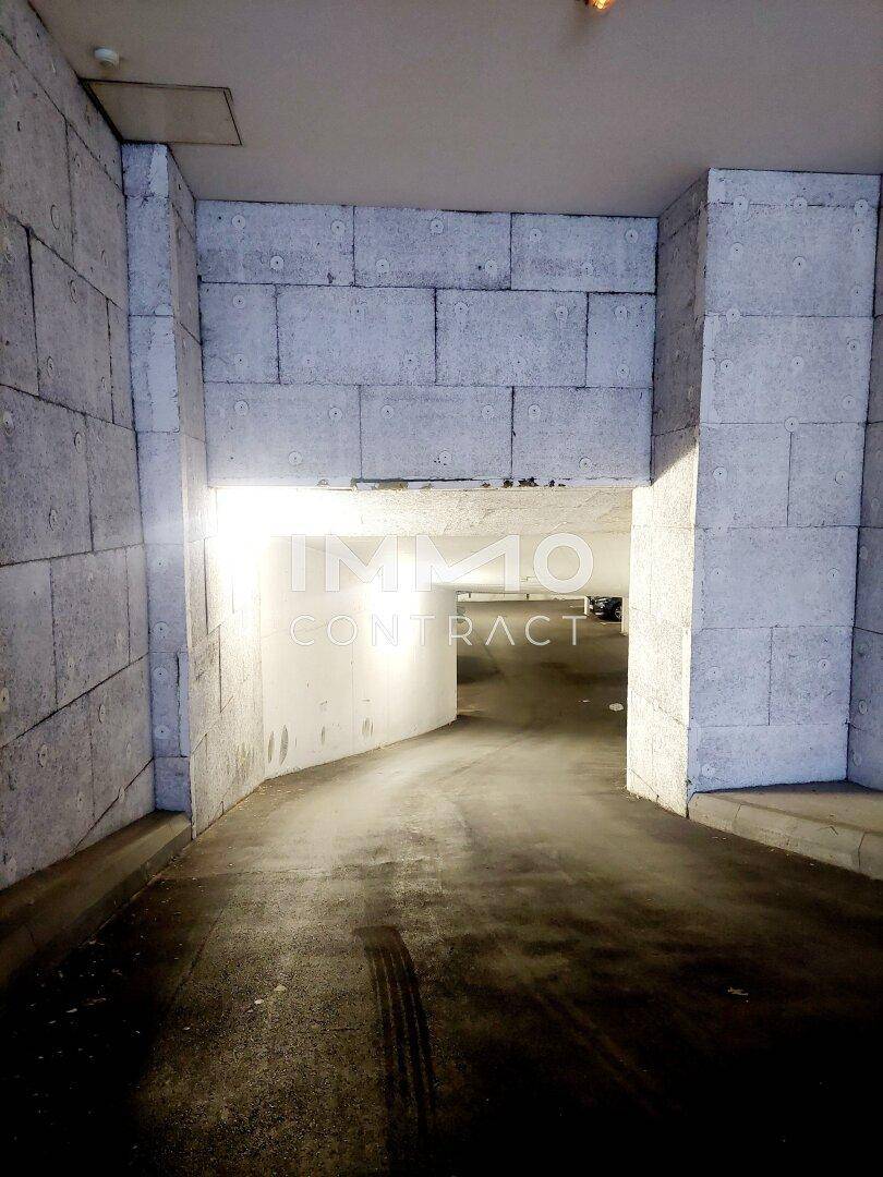 Einfahrt zu einer Tiefgarage mit Betonwänden und heller Beleuchtung am Eingangsbereich.