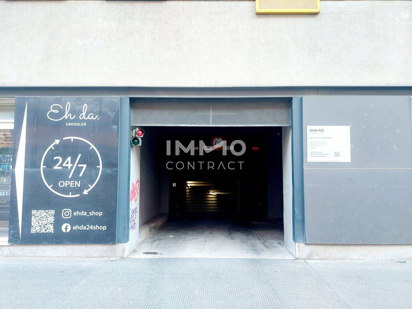 Eingang einer Tiefgarage von der Straße aus gesehen, mit Rolltor und Werbeschildern.