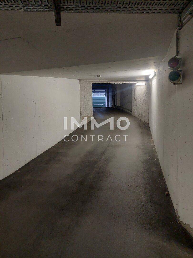Rampe in einer Tiefgarage, die zu weiteren Parkebenen führt, mit Beleuchtung und Verkehrsampel.