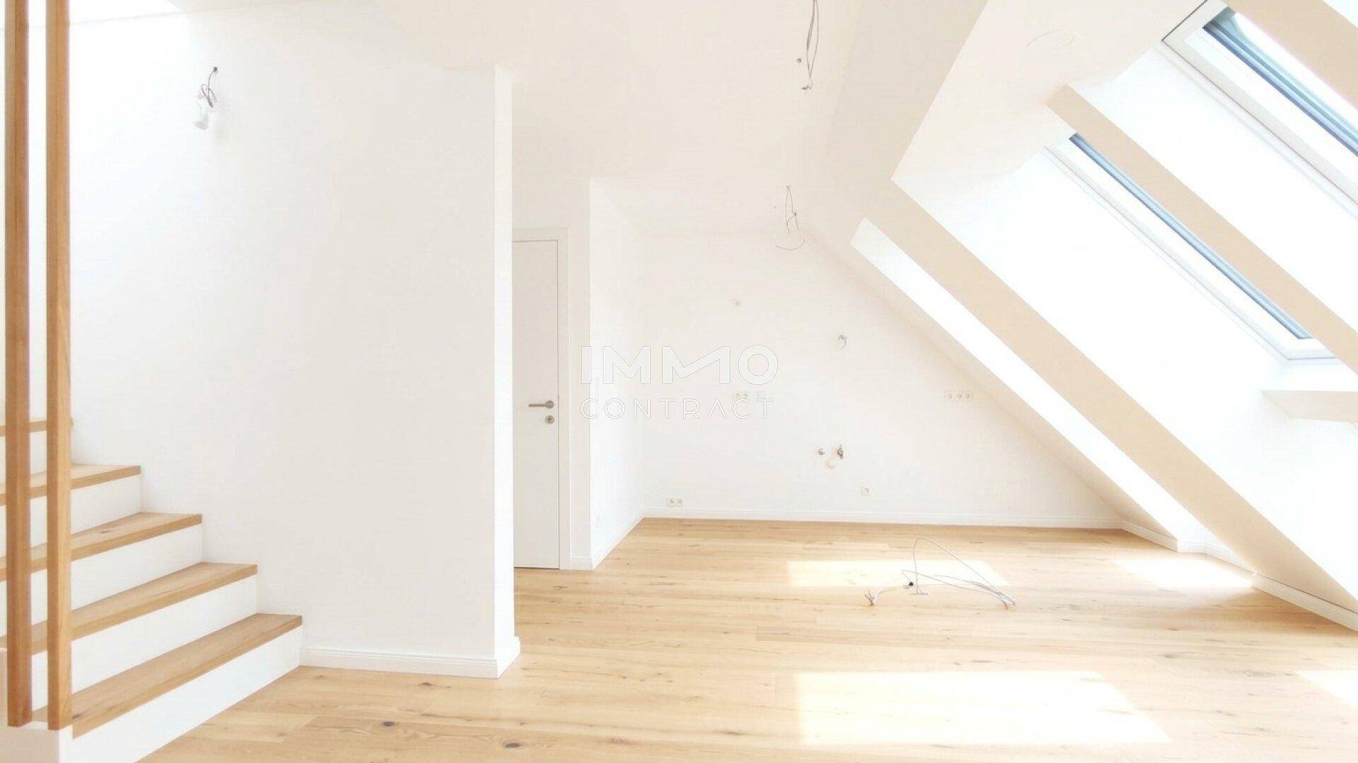 Heller Dachgeschossraum mit Holztreppe, Holzboden und großen Dachfenstern.