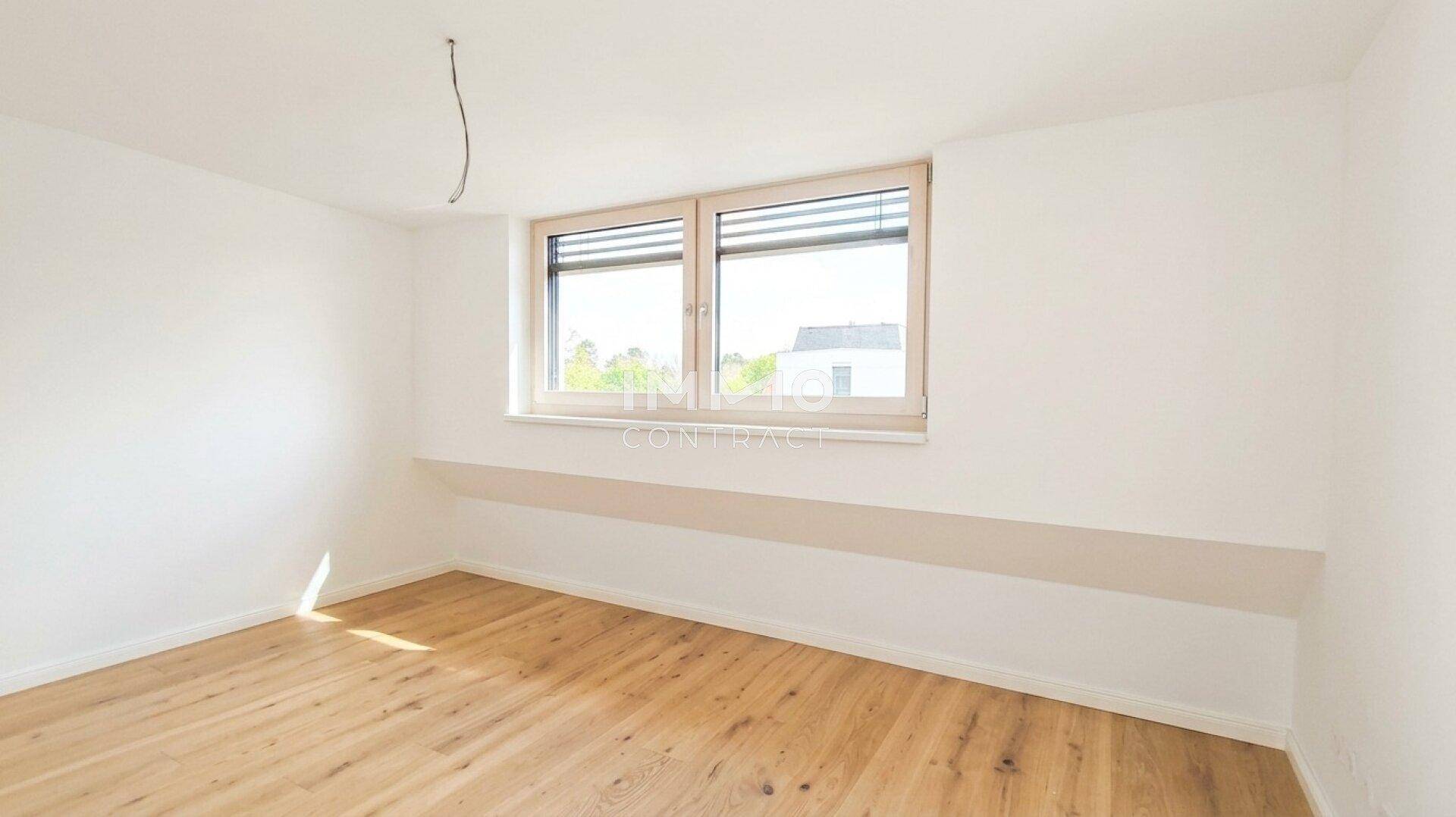 Heller, leerer Raum mit Holzboden und einem großen Fenster.