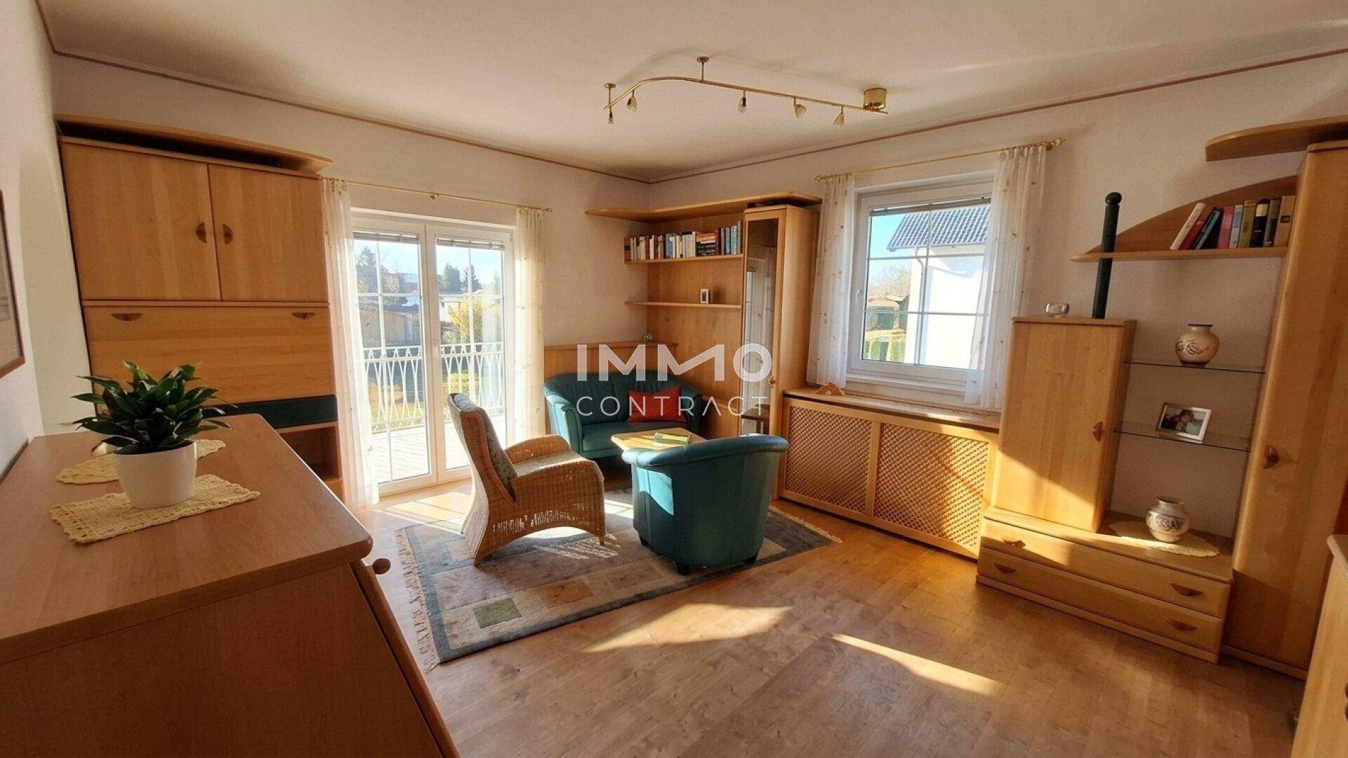 Helles Wohnzimmer mit Holzmöbeln, Korbsessel und Zugang zu einem kleinen Balkon.