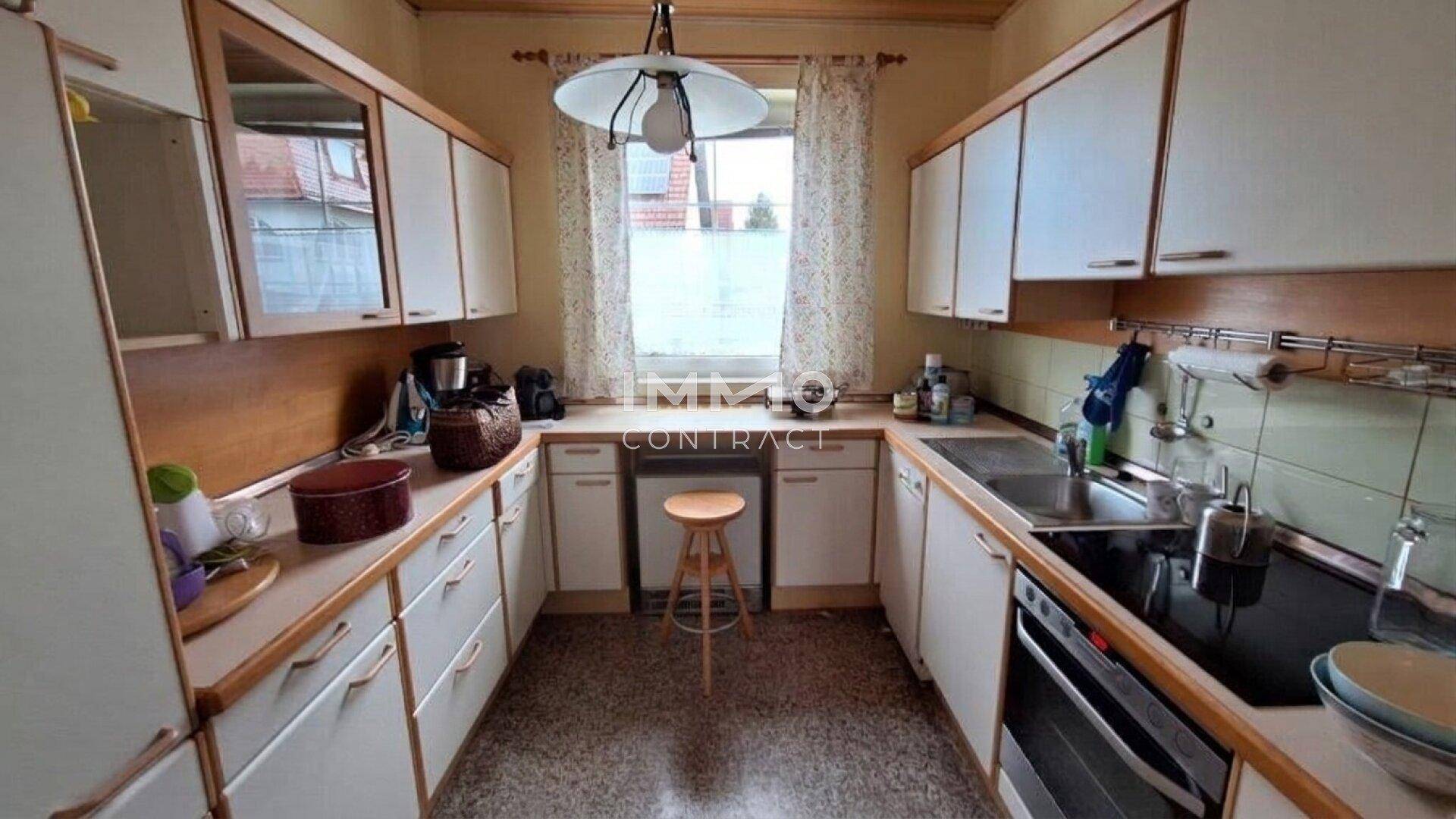 Funktionale Küche mit weißen Schränken, Holzdetails und einem Fenster über der Spüle.
