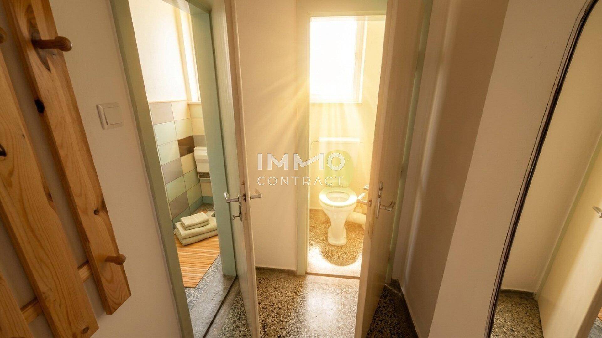 Separates WC mit Fenster und Terrazzoboden, neben einem weiteren Badezimmer.