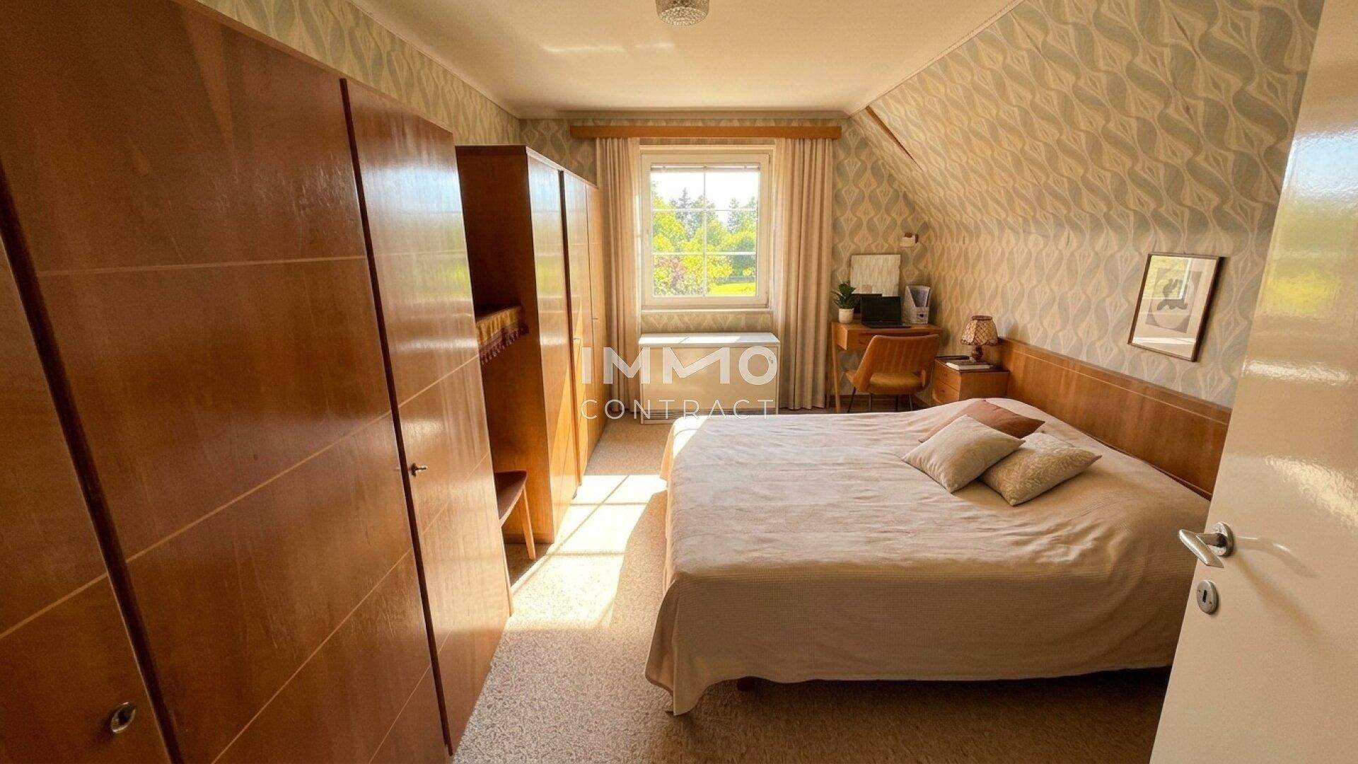 Schlafzimmer mit Doppelbett, Holzschränken und gemusterter Tapete unter Dachschrägen.