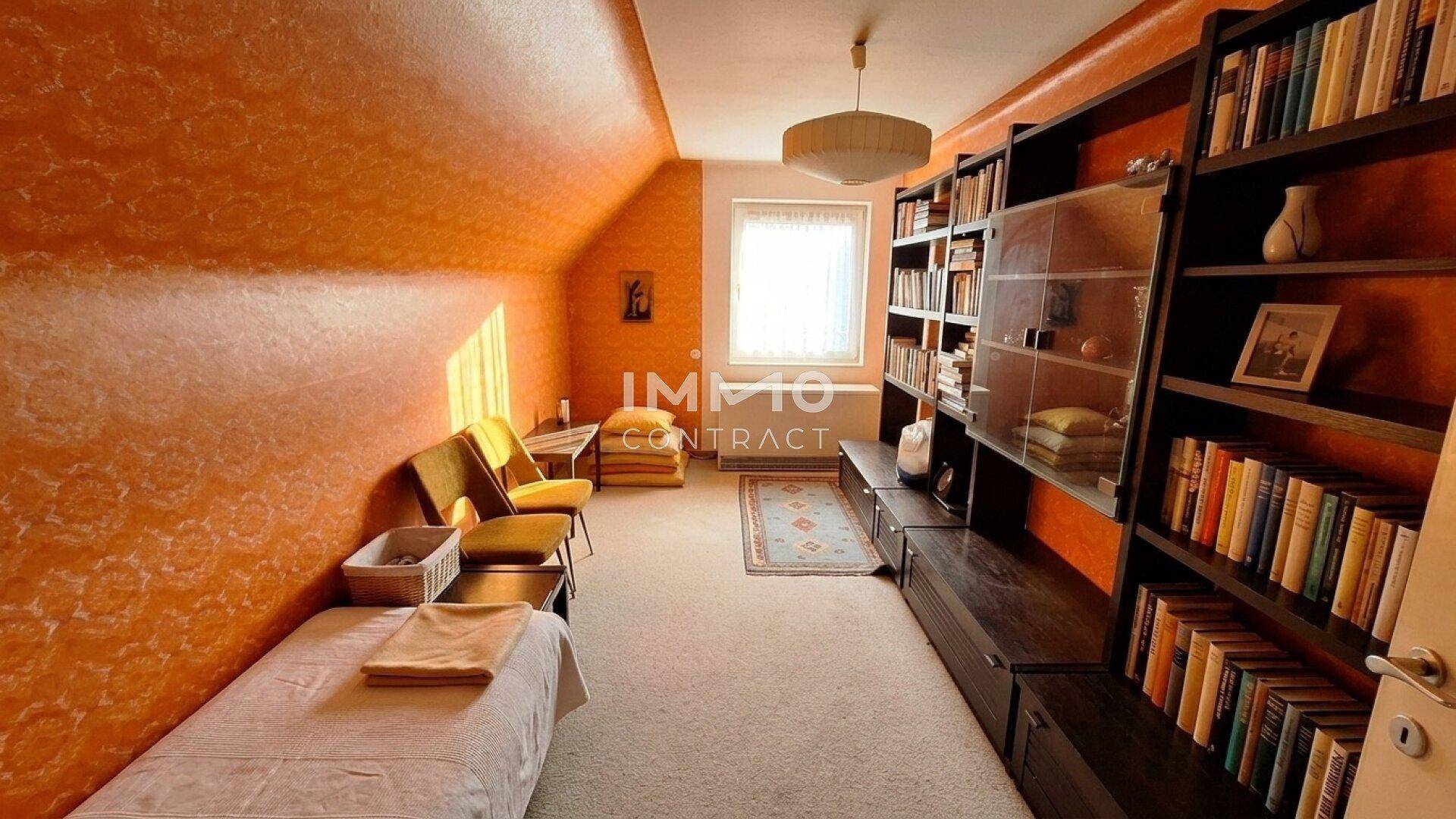 Helles Zimmer mit orangefarbenen Wänden, Bücherregalen und einem Tagesbett unter Dachschrägen.