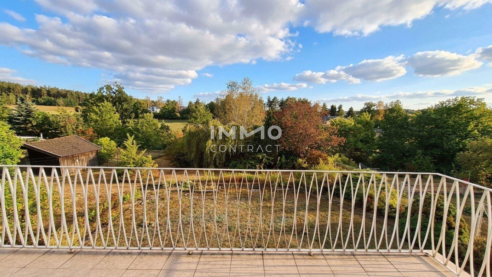 Großer Balkon mit weitem Blick über die grüne Landschaft und Bäume.