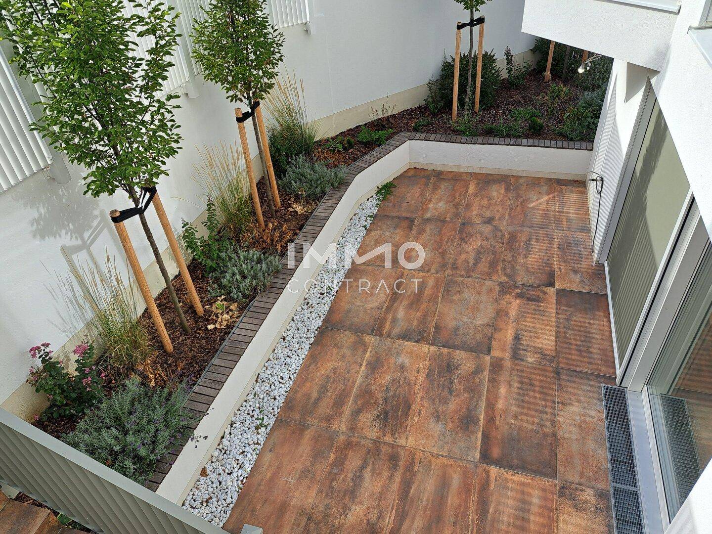 Gepflegter Gartenbereich mit Terrasse, Pflanzenbeeten und jungen Bäumen.