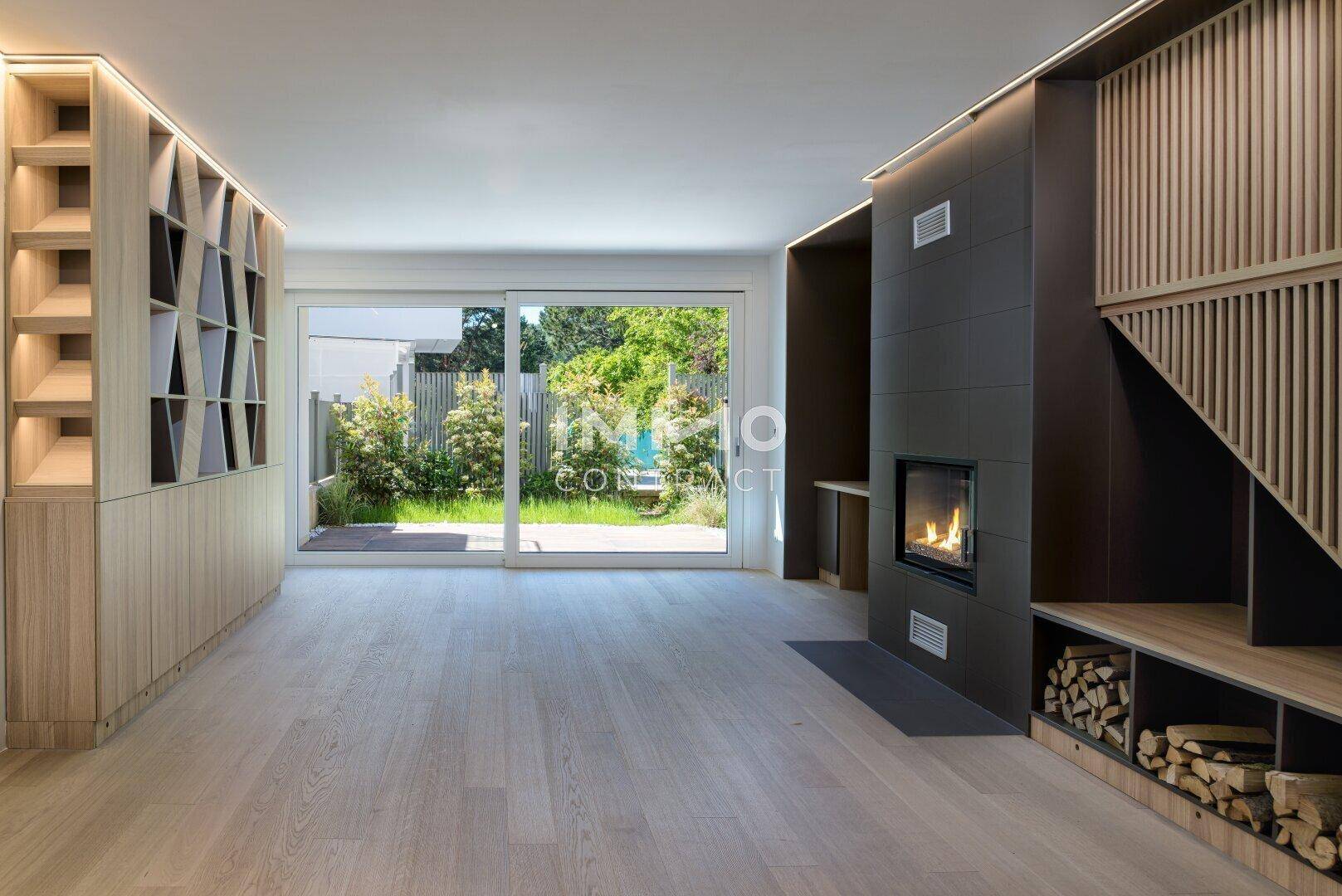 Helles Wohnzimmer mit Holzboden, Kamin und Zugang zu einem grünen Garten.