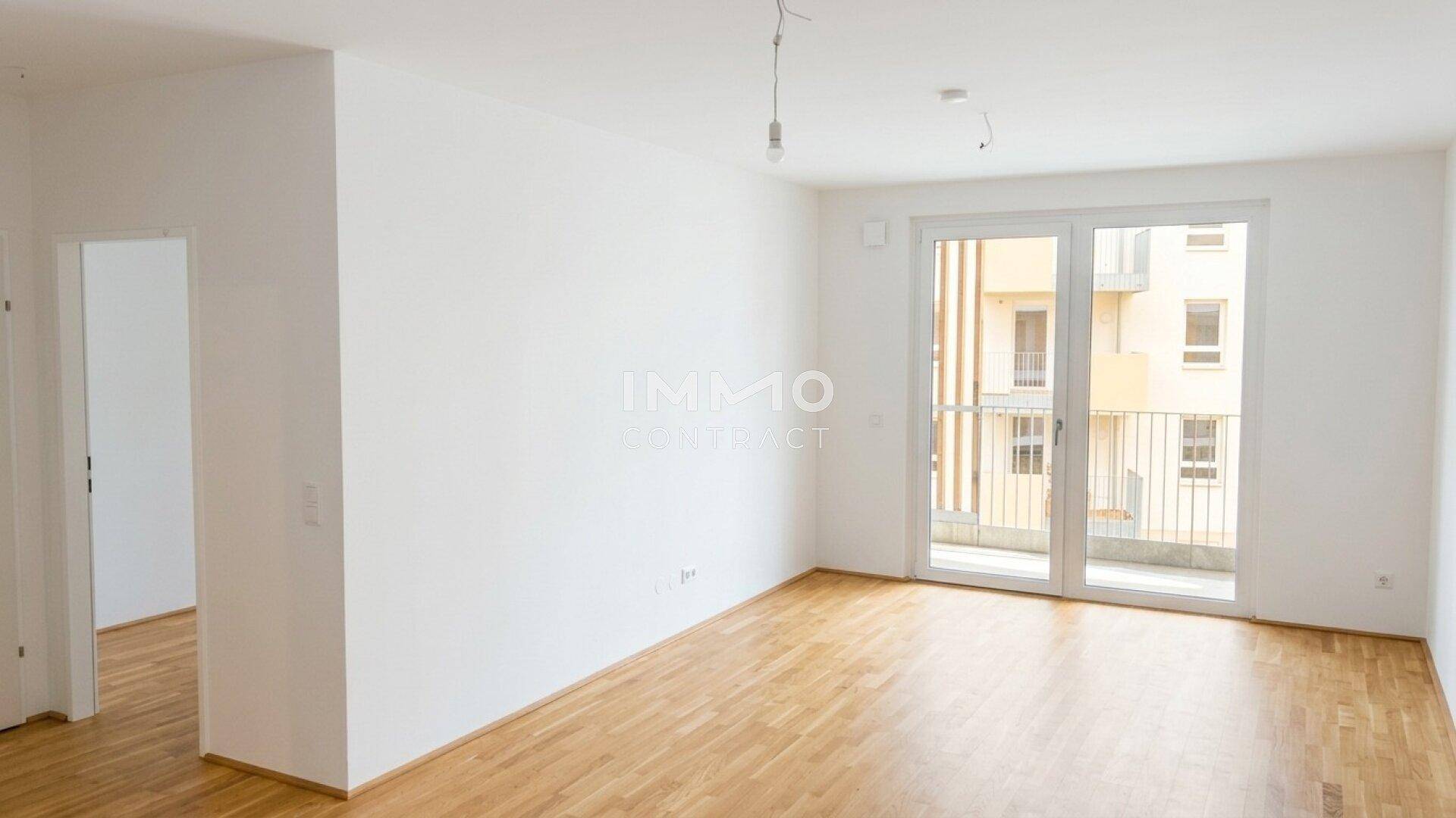 Geräumiges Wohnzimmer mit hellem Parkettboden und Zugang zu einem Balkon, bereit zur Einrichtung.