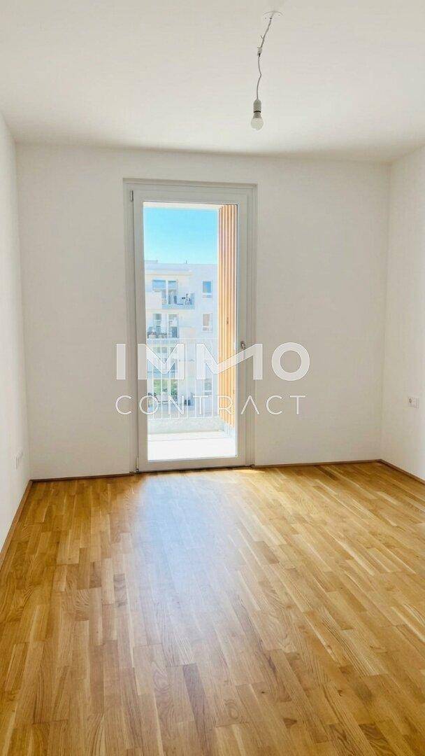 Lichtdurchfluteter Raum mit Parkettboden und großem Fenster, das viel Tageslicht hereinlässt.