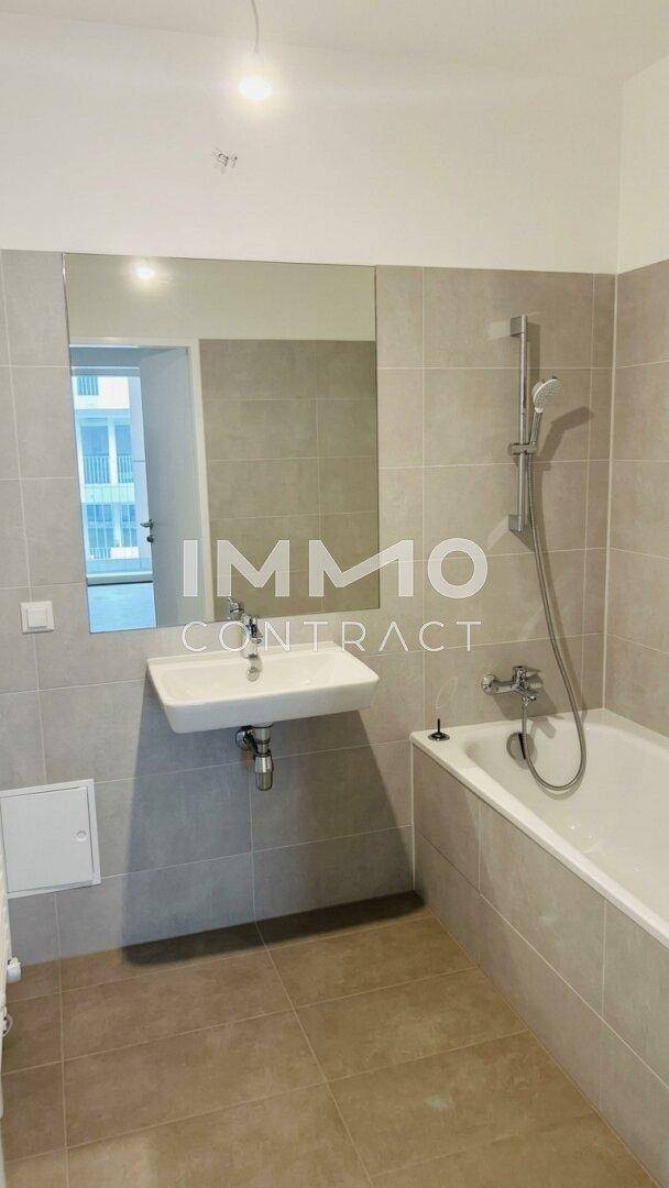 Modernes Badezimmer mit Badewanne, Waschbecken und großem Spiegel, hell gefliest.