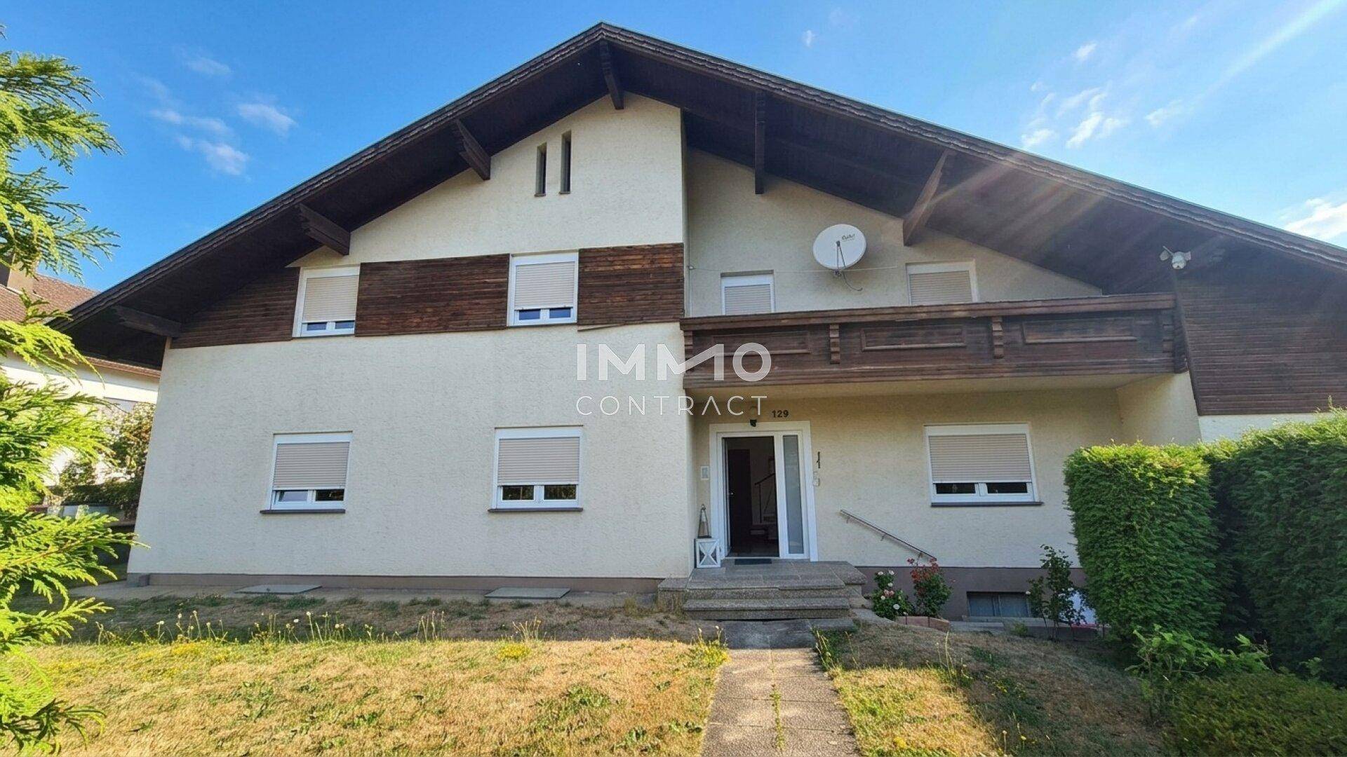 Vorderansicht eines Einfamilienhauses mit Satteldach, Balkon und Vorgarten.