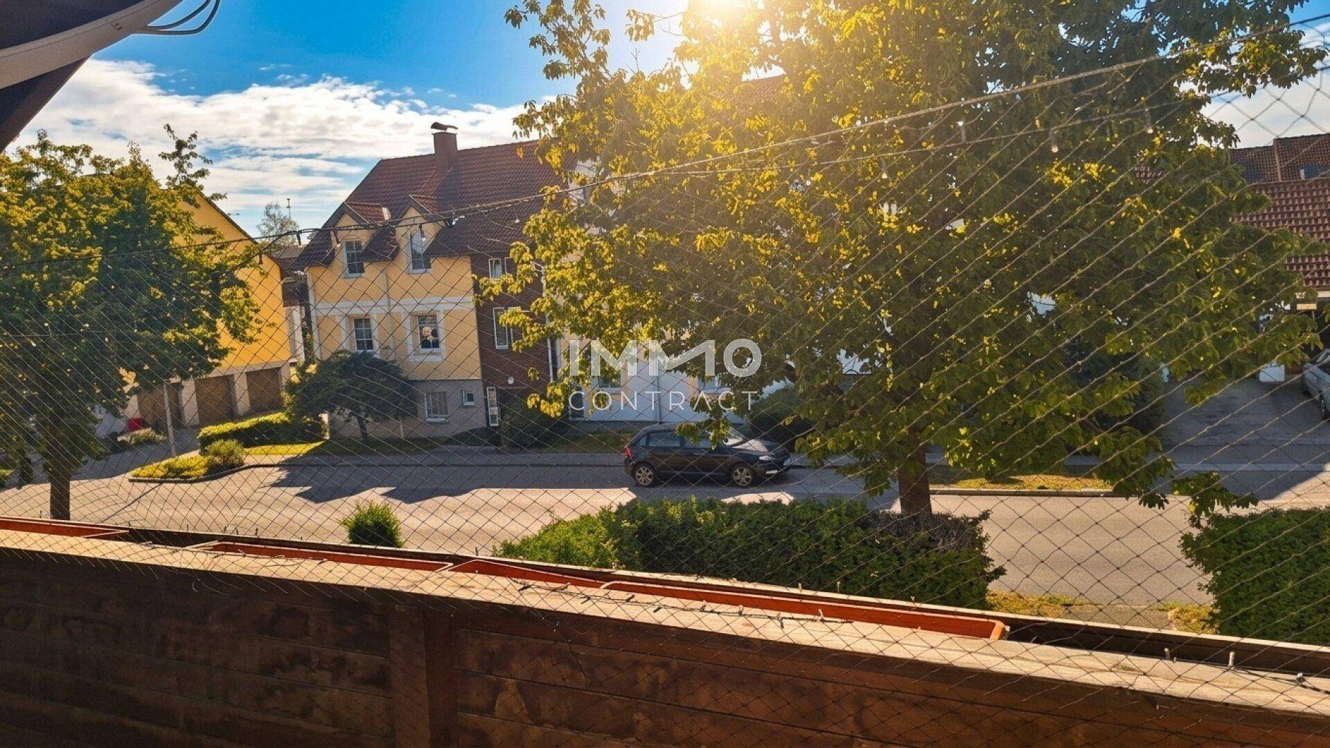 Sonniger Ausblick vom Balkon auf eine ruhige Wohnstraße mit Bäumen und Häusern.