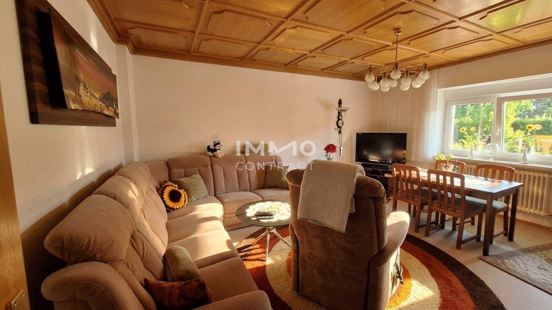 Gemütlicher Wohn-Essbereich mit Holzkassettendecke, Ecksofa und Esstisch am Fenster.