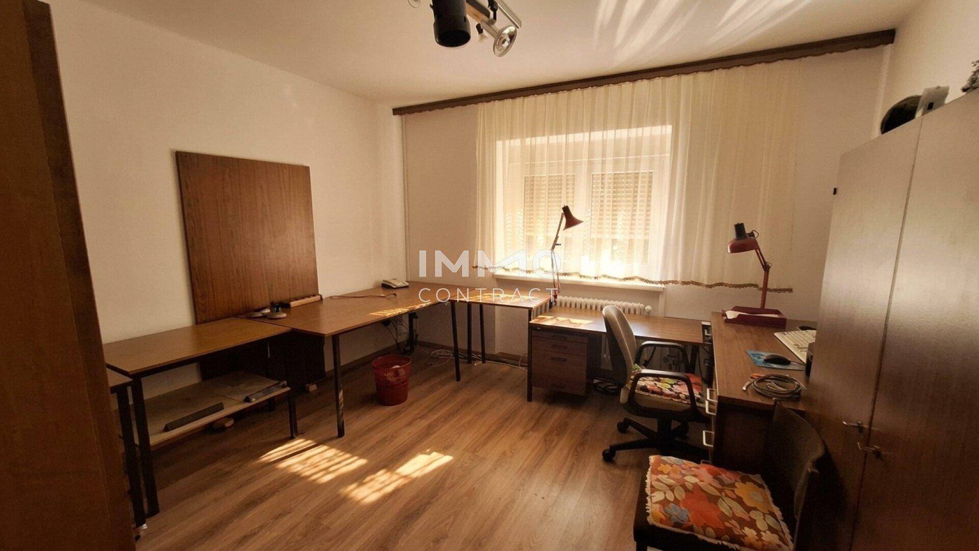 Helles Arbeitszimmer mit Holzfußboden, mehreren Schreibtischen und großem Fenster.