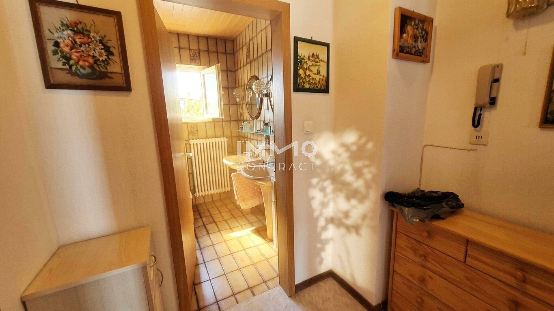 Flur mit Blick in ein gefliestes Badezimmer mit Fenster und Waschbecken.