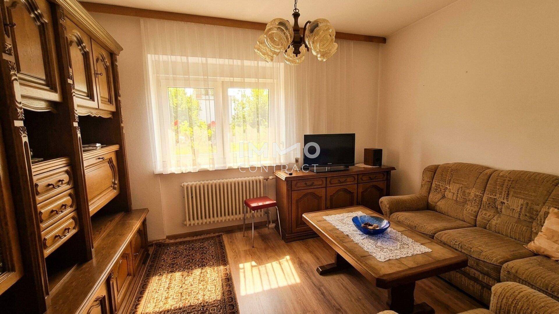 Wohnzimmer mit traditionellen Holzmöbeln, Sofa und Fenster mit Blick ins Grüne.