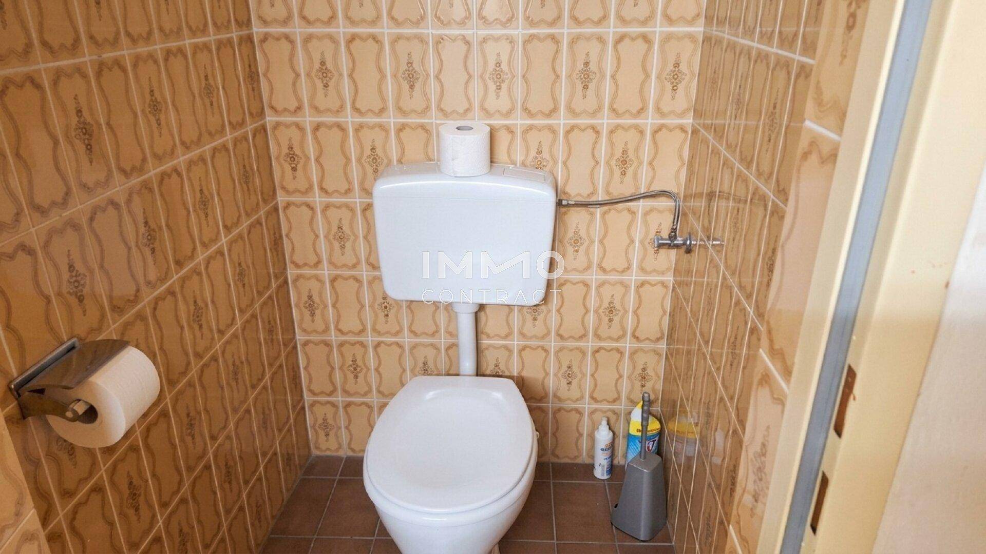 Separate Toilette mit braunen Fliesen und Standard-WC-Becken.