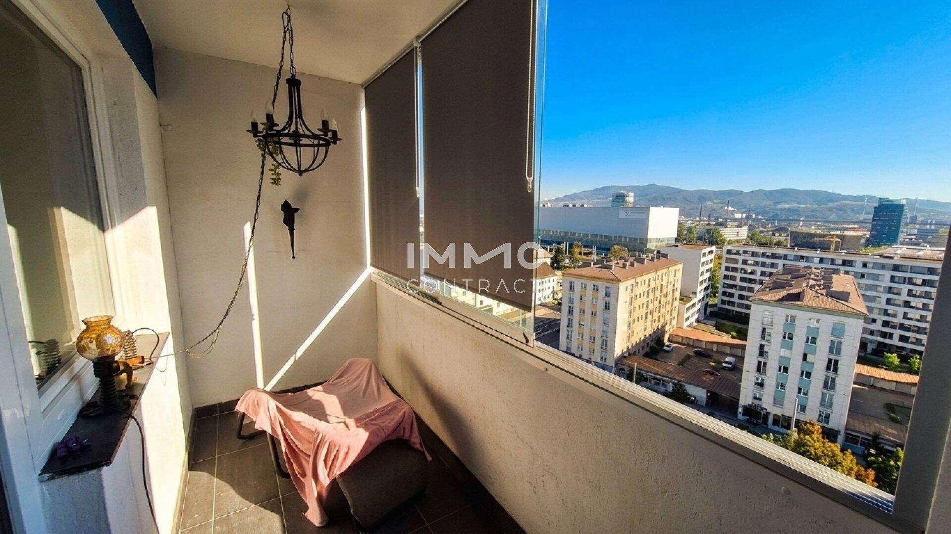 Balkon mit Stadtblick und fernen Bergen, ausgestattet mit einem Stuhl und einem kleinen Tisch.