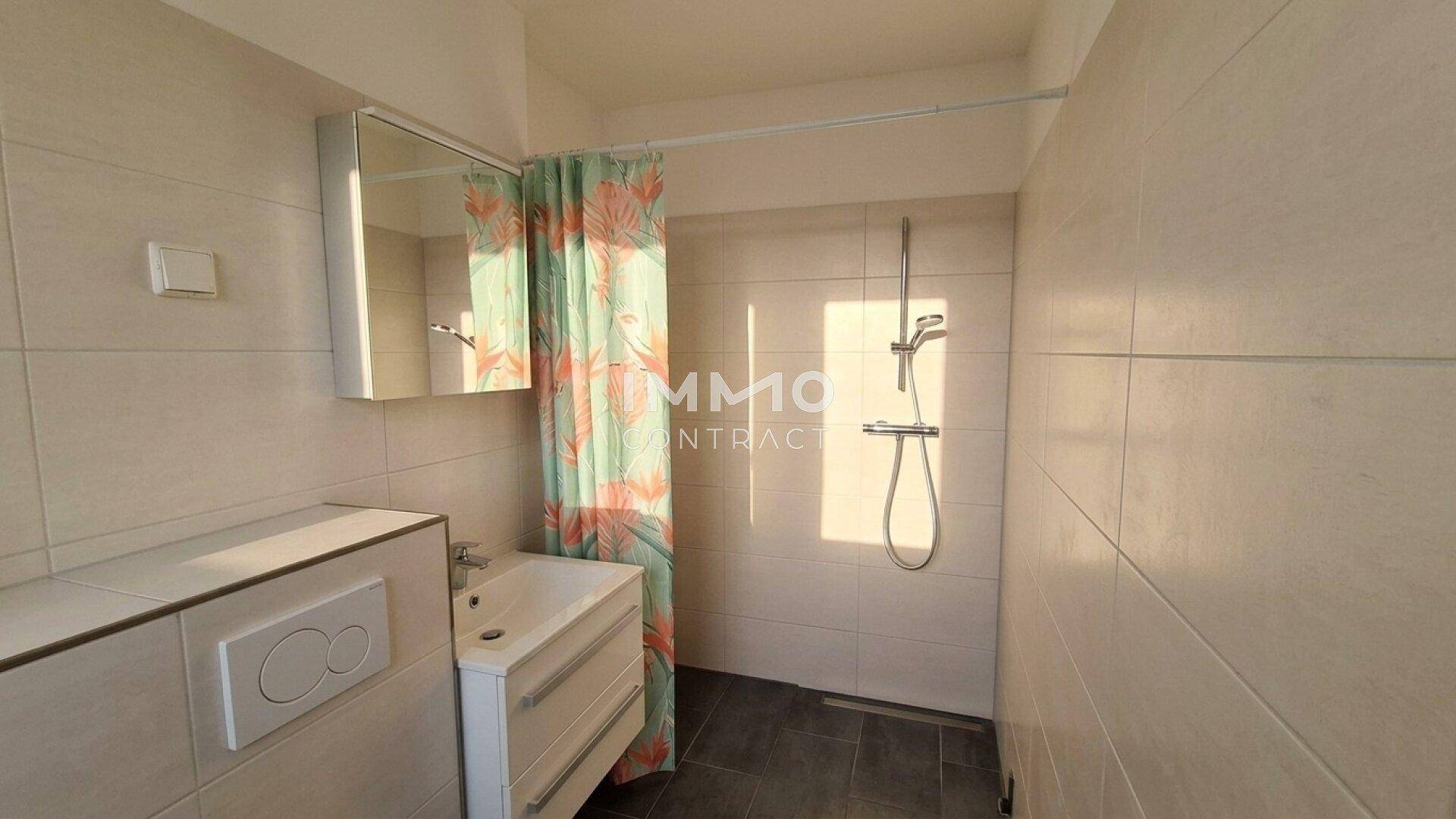 Modernes Badezimmer mit Dusche, Waschbecken und WC, hell gefliest.