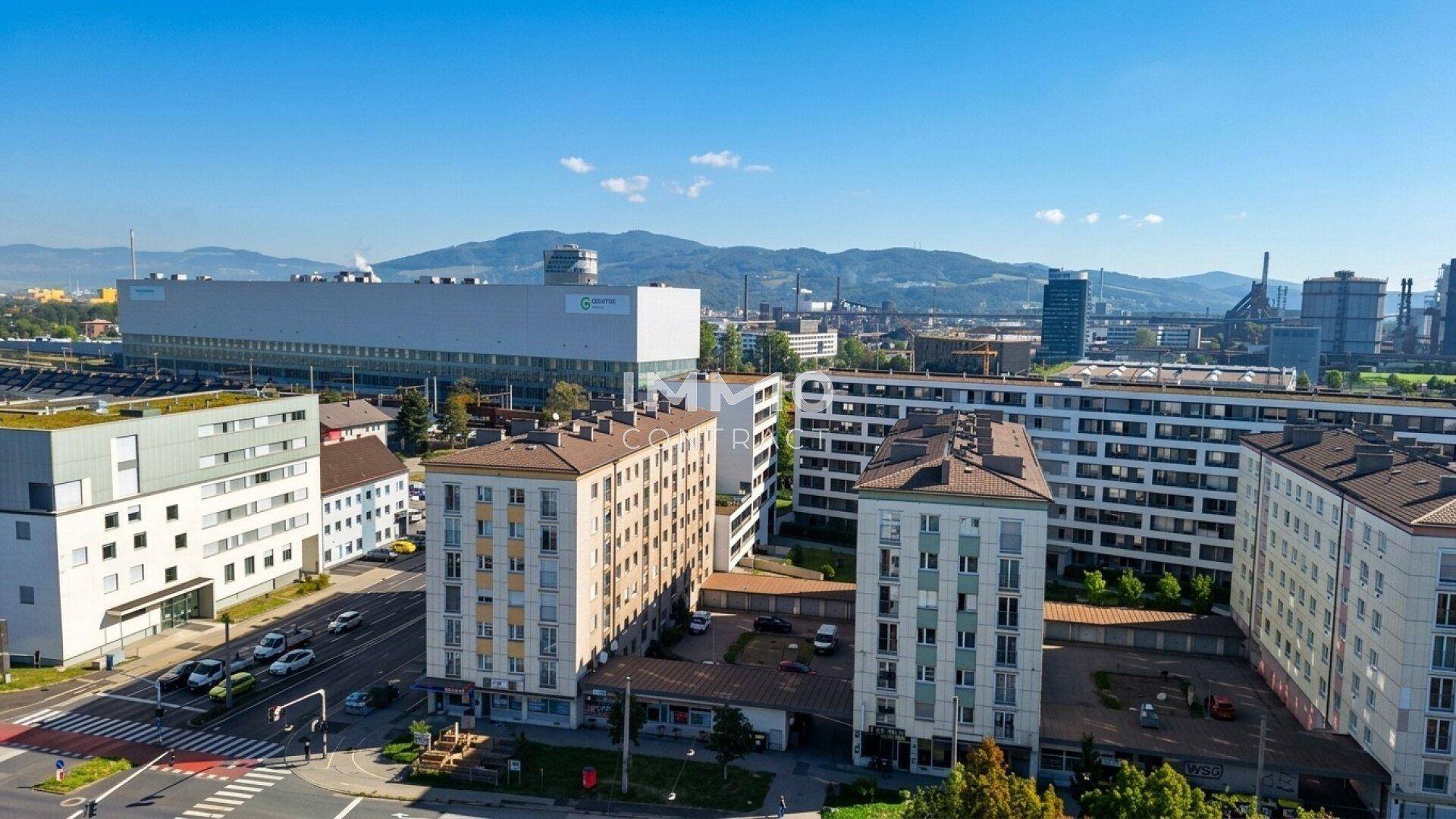 Luftaufnahme eines Stadtviertels mit Wohngebäuden, Straßen und Bergen im Hintergrund.