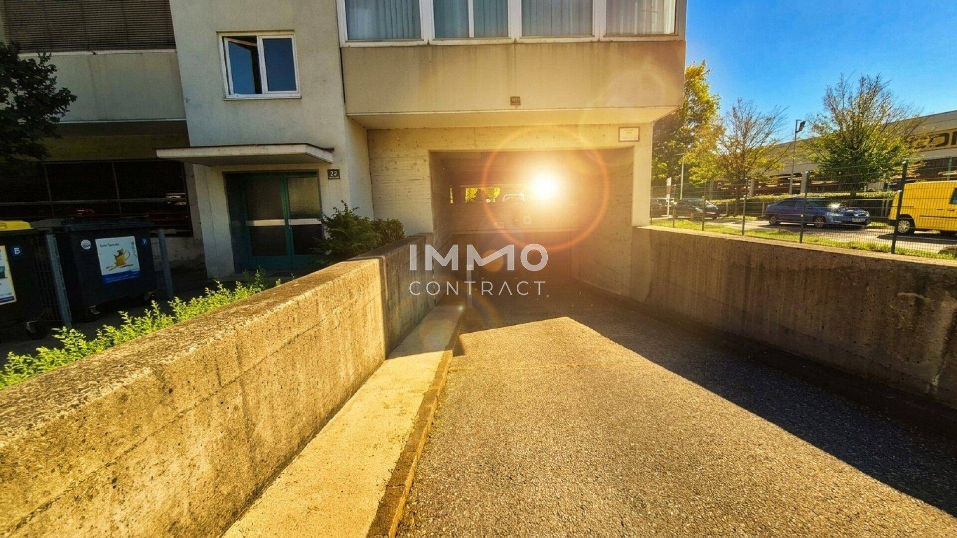 Einfahrt zu einer Tiefgarage mit Rampe und Gebäudeeingang im Hintergrund.