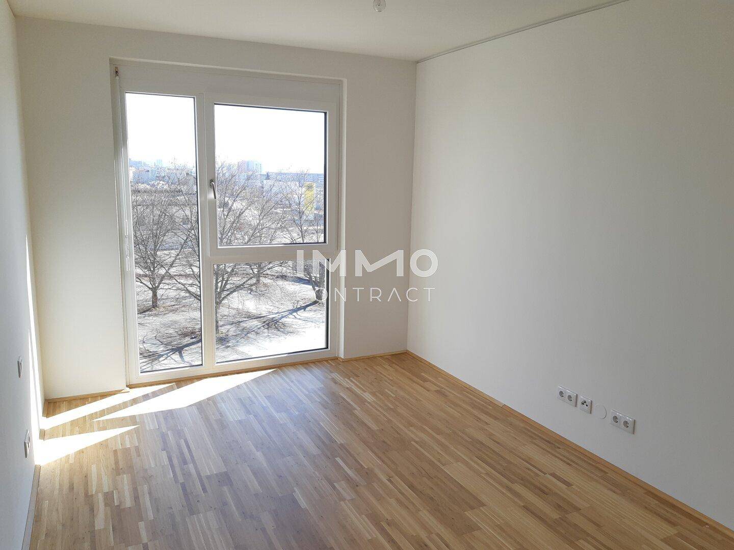 Heller Raum mit Holzboden und großem Fenster mit Blick ins Grüne.