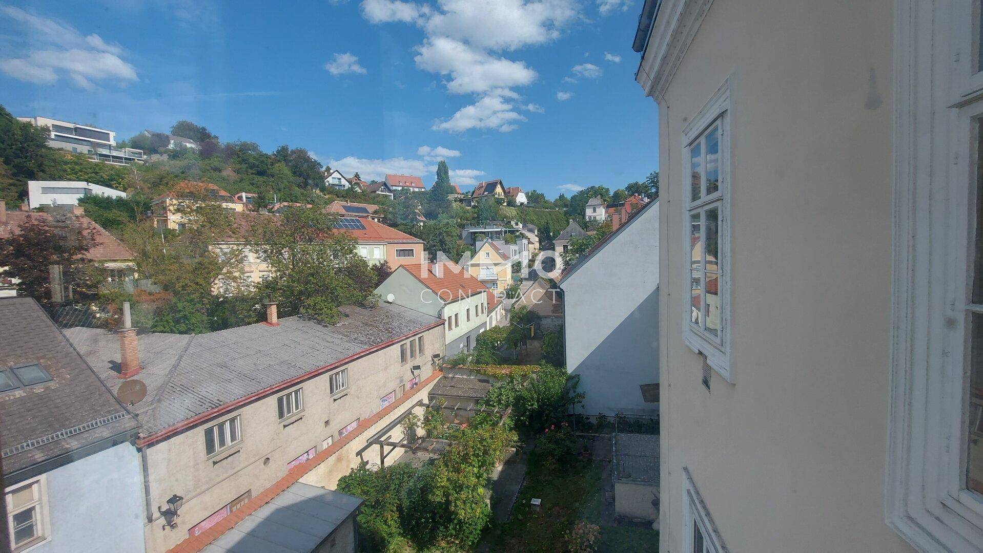 Weitblick über die Dächer der Nachbarschaft und grüne Hügel unter blauem Himmel.