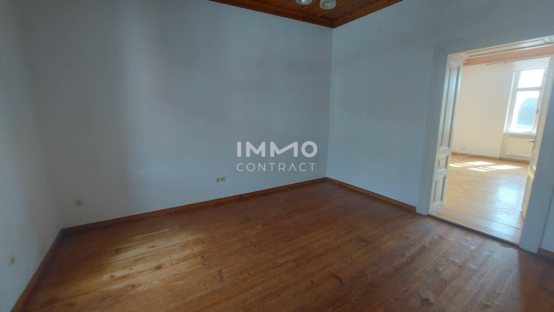 Schlichtes Zimmer mit Holzdielenboden und weiß gestrichenen Wänden, bereit zur individuellen Gestaltung.