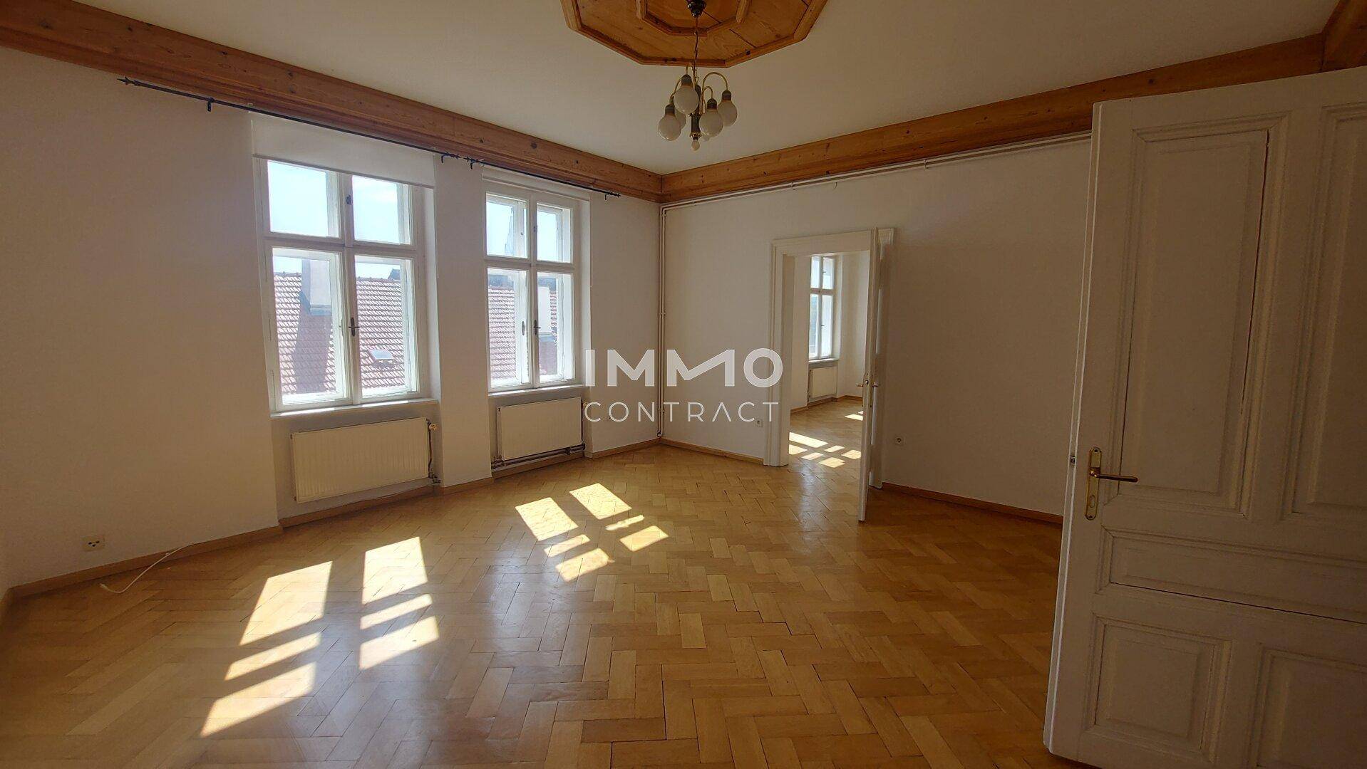 Geräumiges Wohnzimmer mit Fischgrätparkett, Holzbalken und einem dekorativen Deckenmedaillon.