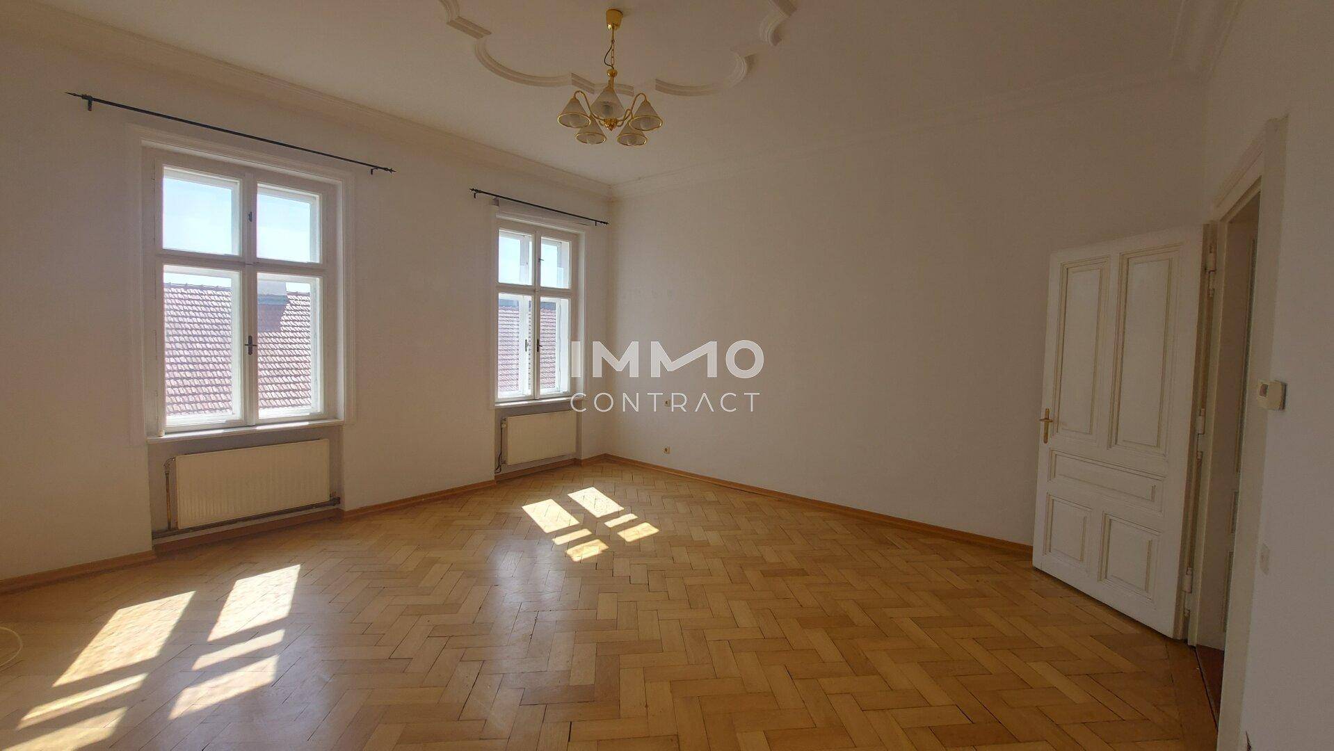 Lichtdurchflutetes Zimmer mit Fischgrätparkett, hohen Decken und einem eleganten Stuckdeckenmedaillon.