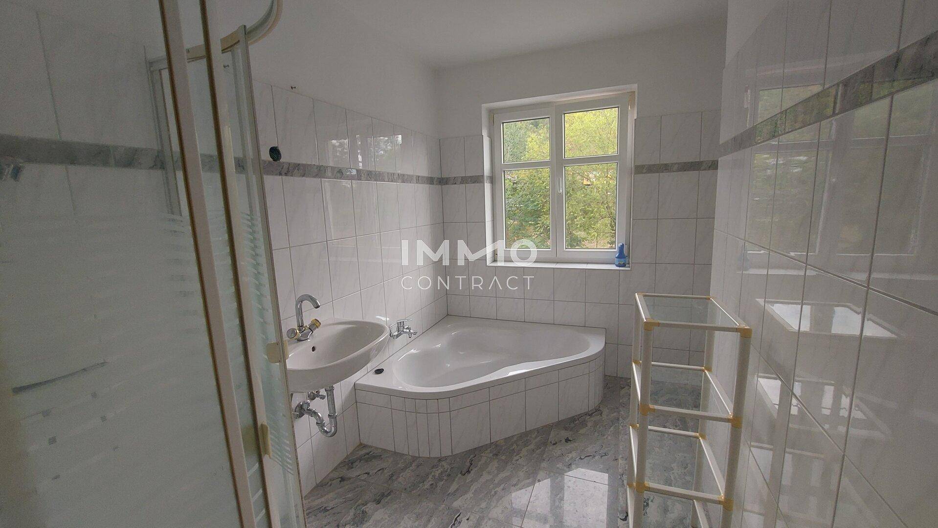 Gefliestes Badezimmer mit Badewanne, Dusche und Fenster, bietet ausreichend Tageslicht.