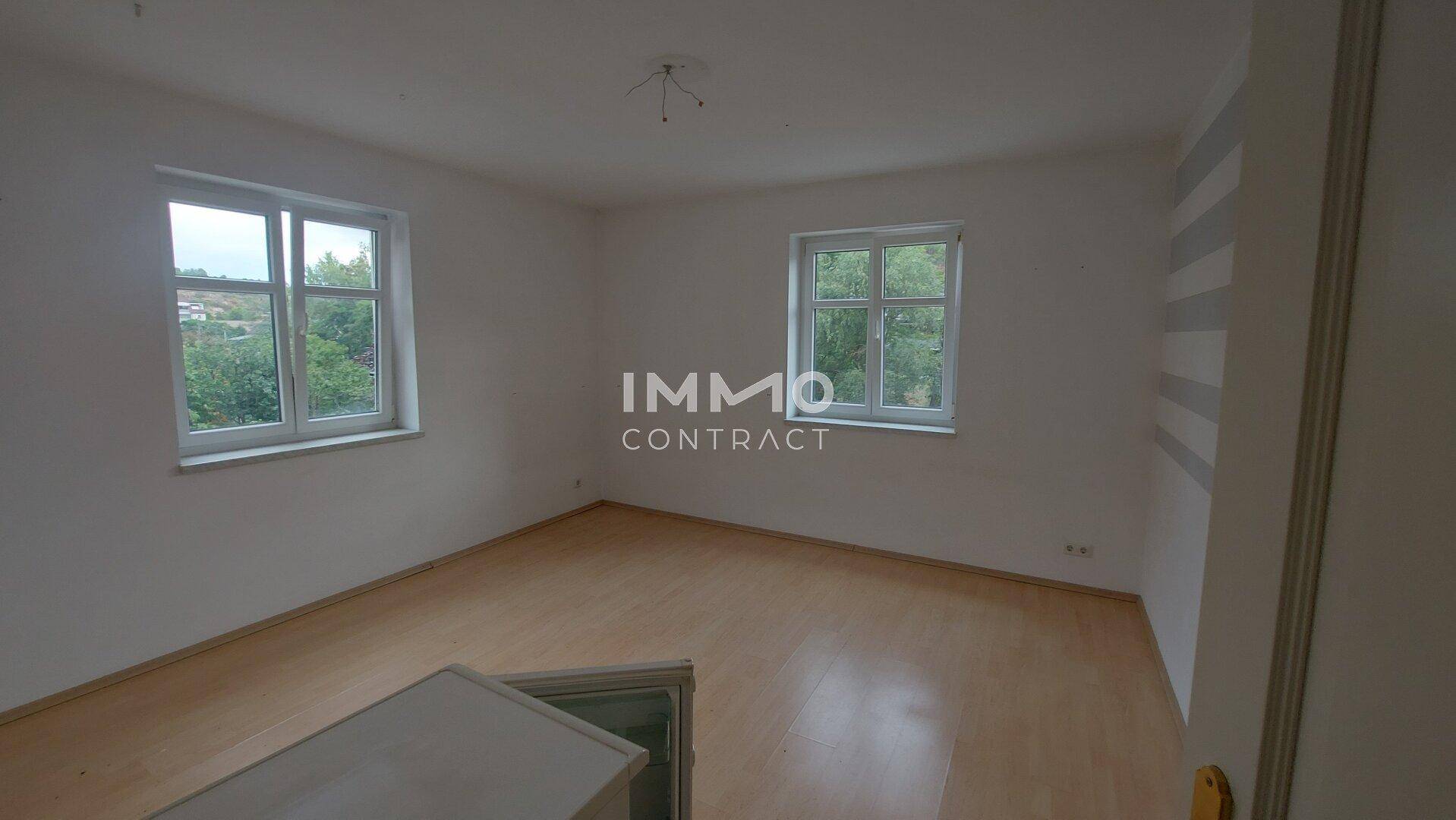 Schlafzimmer mit Holzboden und zwei Fenstern, die für eine helle und freundliche Atmosphäre sorgen.