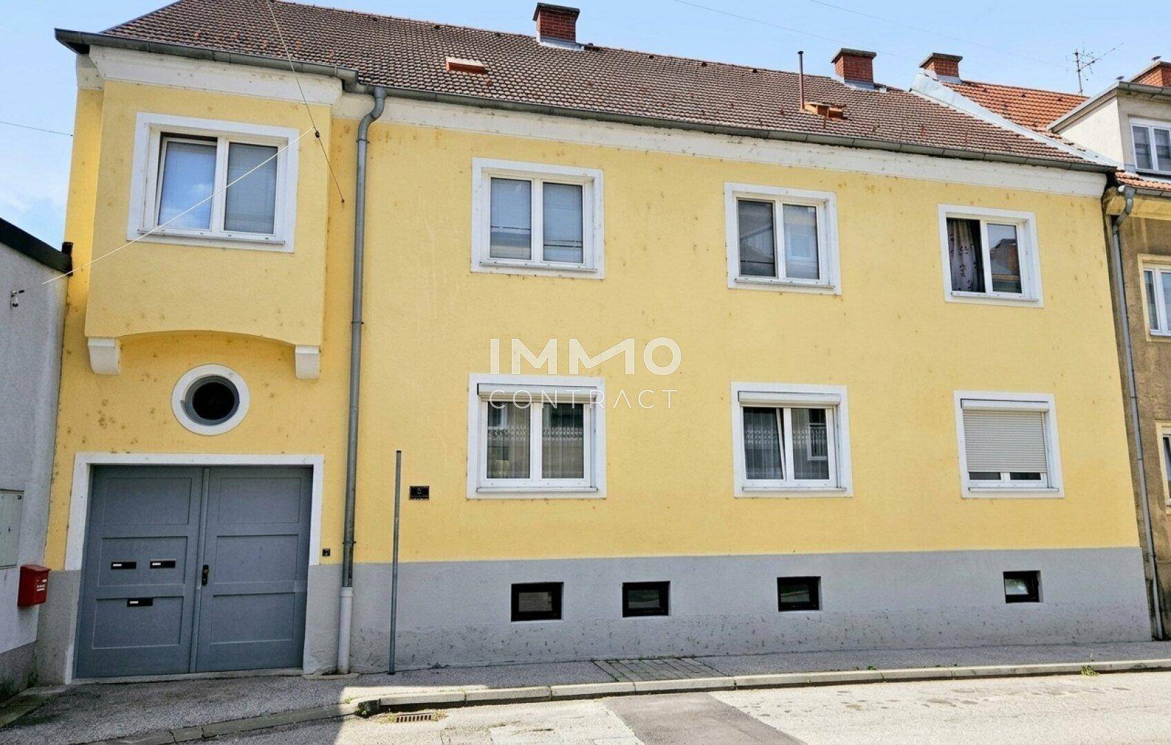 Vorderansicht des gelben Gebäudes mit mehreren Fenstern, einem Garagentor und Rollläden.