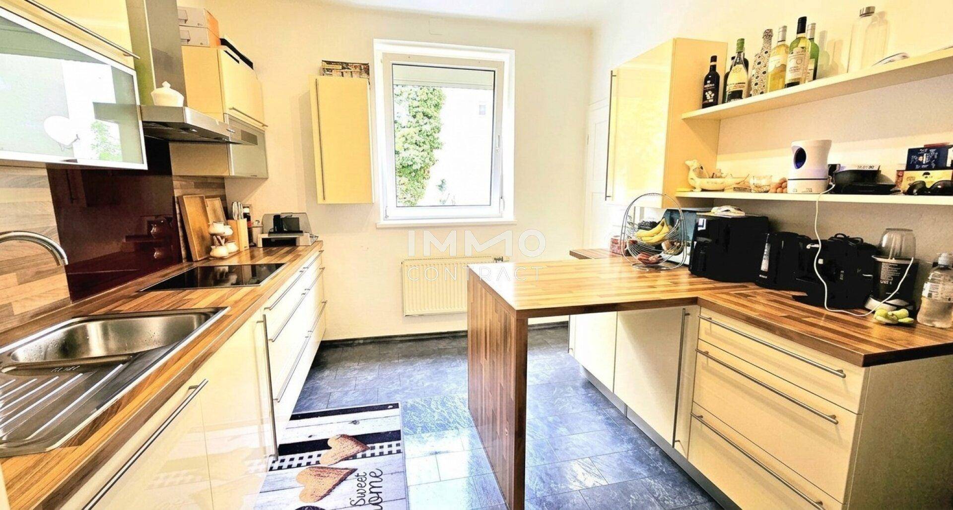 Helle Küche mit Holz-Arbeitsplatten, hellen Schränken, Fliesenboden und einem Fenster.