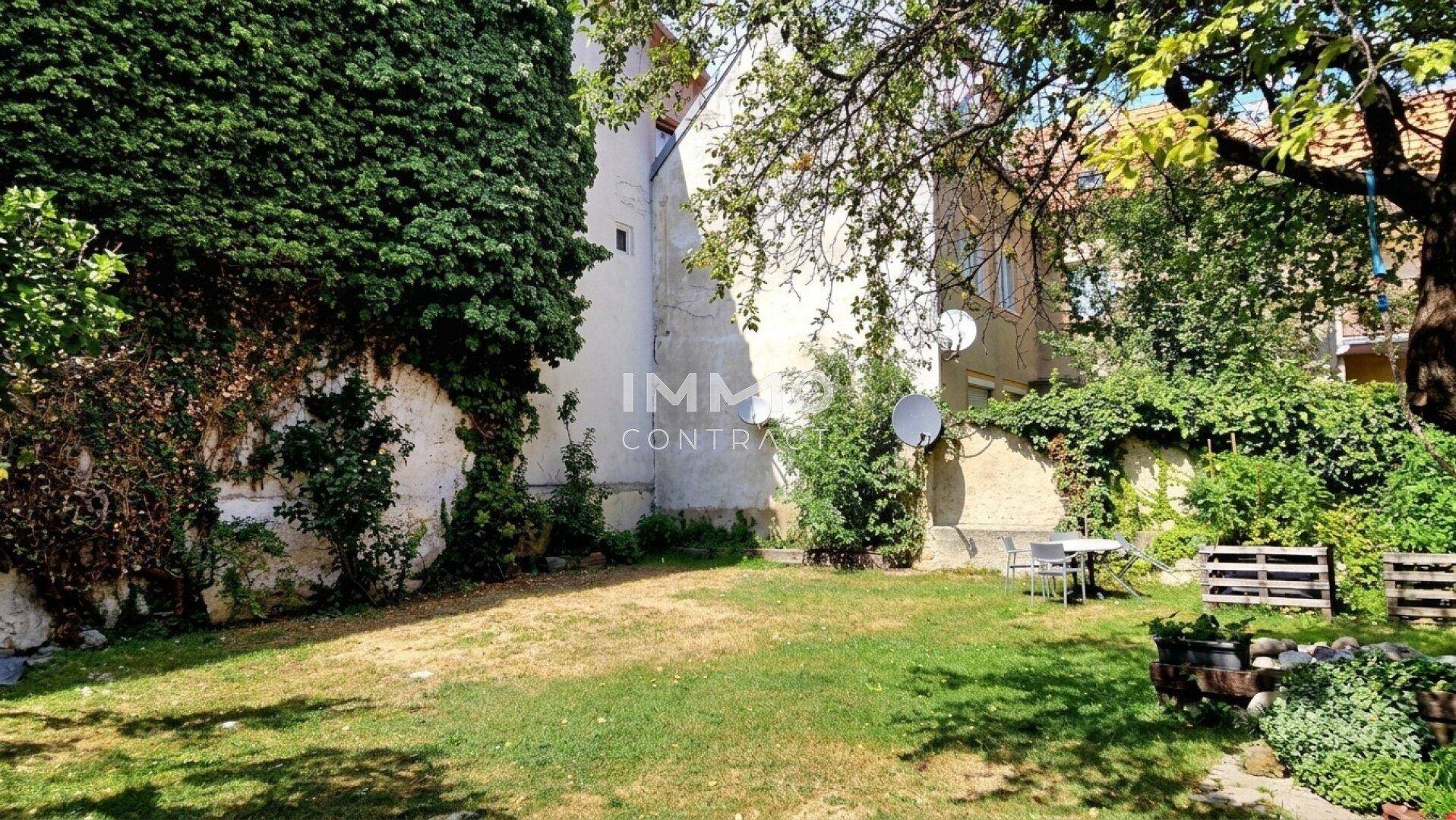 Grüner Gartenbereich mit Efeu bewachsenen Mauern, Rasen und einer kleinen Sitzgelegenheit im Freien.